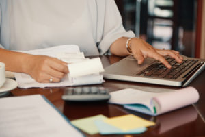 A woman multitasking as a CPA by typing on a laptop and holding a cup of coffee.