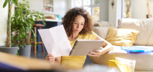 A woman is sitting on a couch, providing accounting services while looking at a tablet.