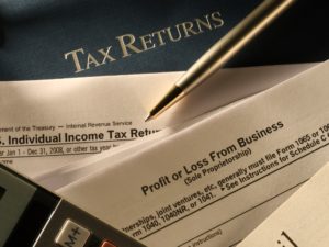 Tax professional preparing tax returns with calculator and pen on desk.