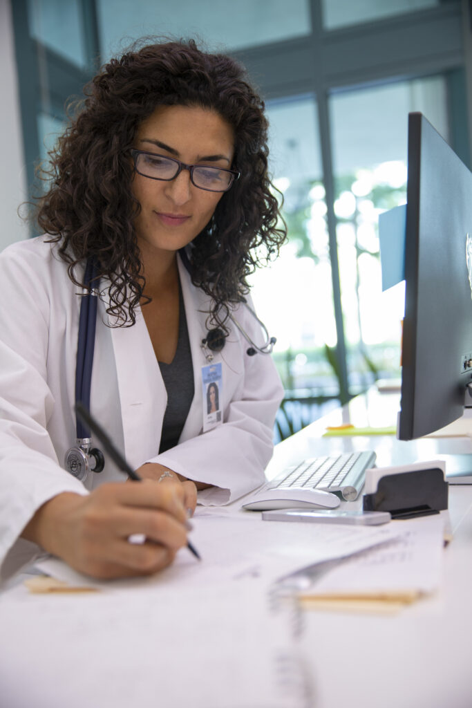 A female doctor in a lab coat accurately tracking medical expenses on a piece of paper.
