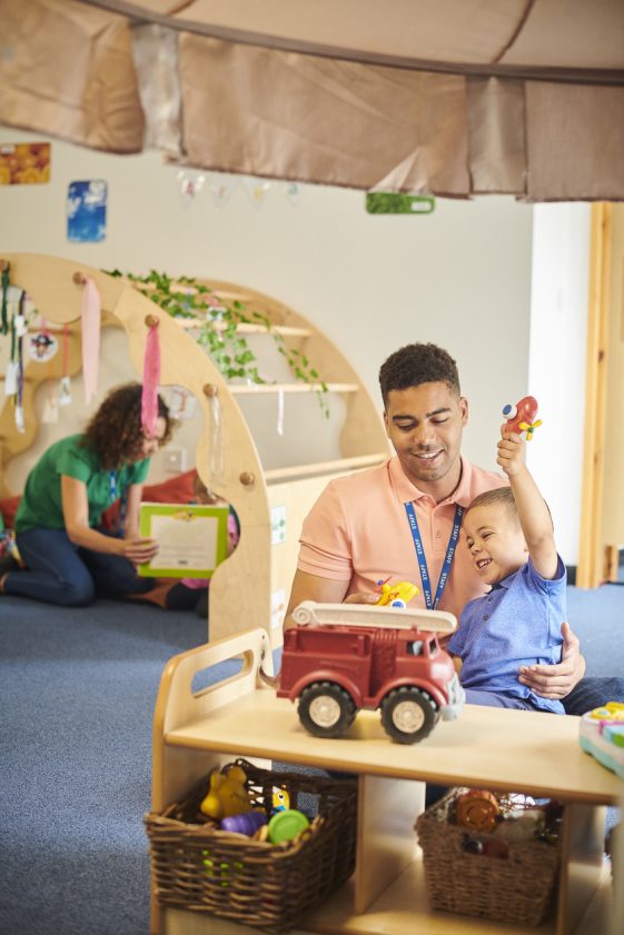 A man manages accounting services for daycare companies in a playroom with a child.